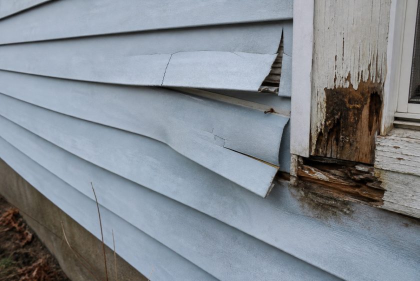 Cracked and warped old siding with rotted trim, a clear sign siding replacement is needed